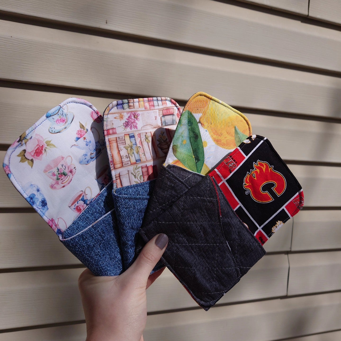 Hand holding four fabric pouches with different designs on a wooden surface
