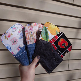 Hand holding four fabric pouches with different designs on a wooden surface
