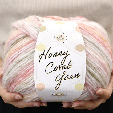 Ball of yarn with a label reading 'Honey Comb Yarn' held by hands.