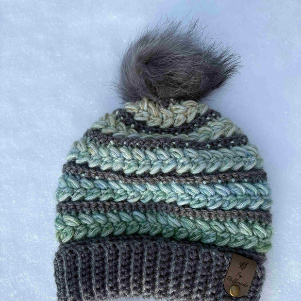 Crochet beanie and glove set with fur pom-pom on a snowy background